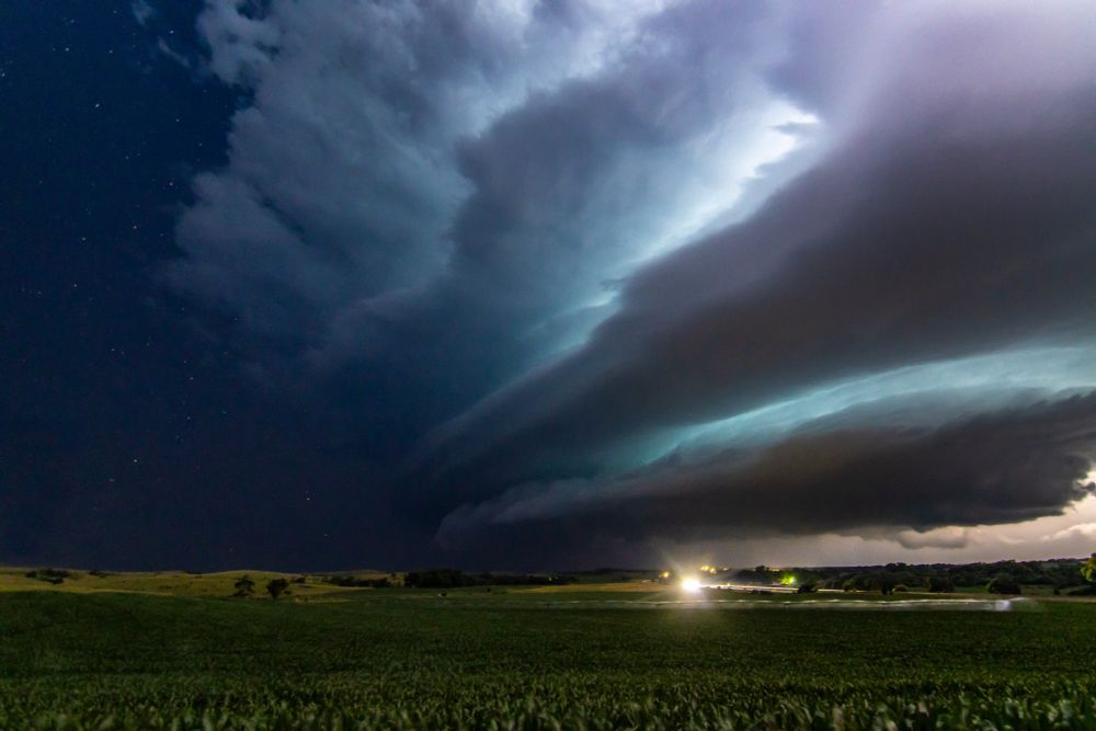 Photo of a supercell thunderstorm illuminated by lightning with stars above over a rural farm field near Broken Bow, Nebraska on July 11, 2023.