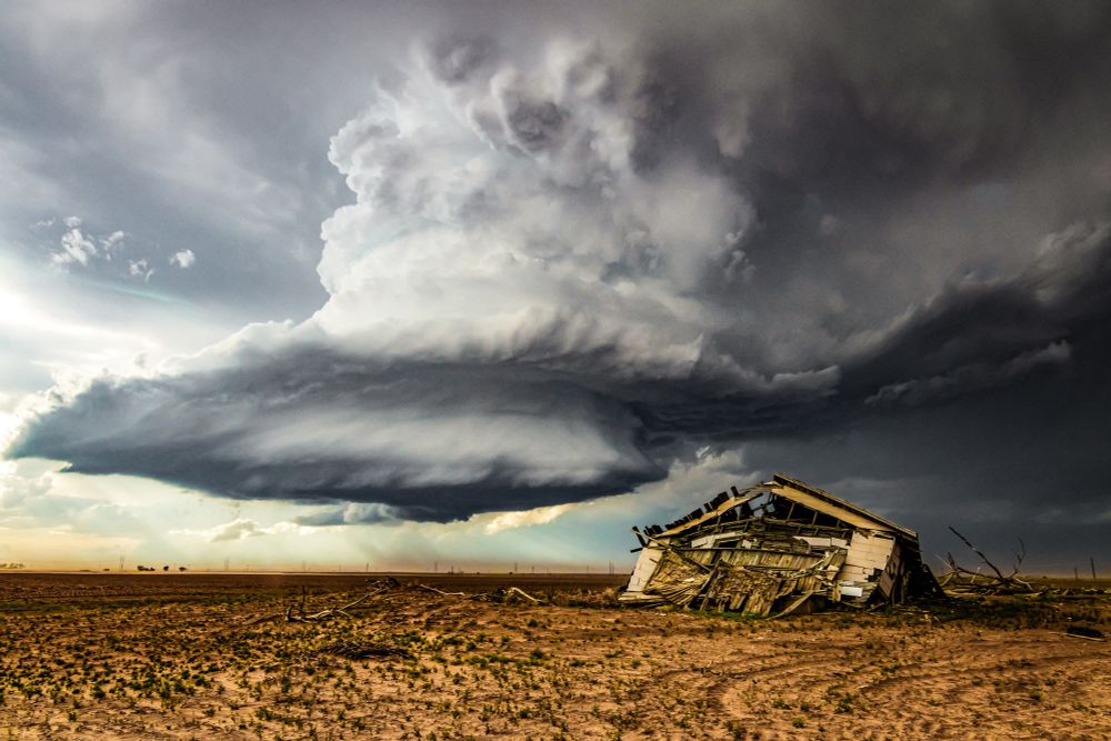 Photo of a supercell thunderstorm over orange/brown landscape and an abandoned building near Lubbock, Texas on May 17, 2021.