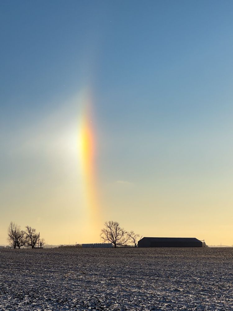 Sundog over a rural snow covered field, a farm building, and trees after sunrise in Watertown, SD on December 11, 2024.