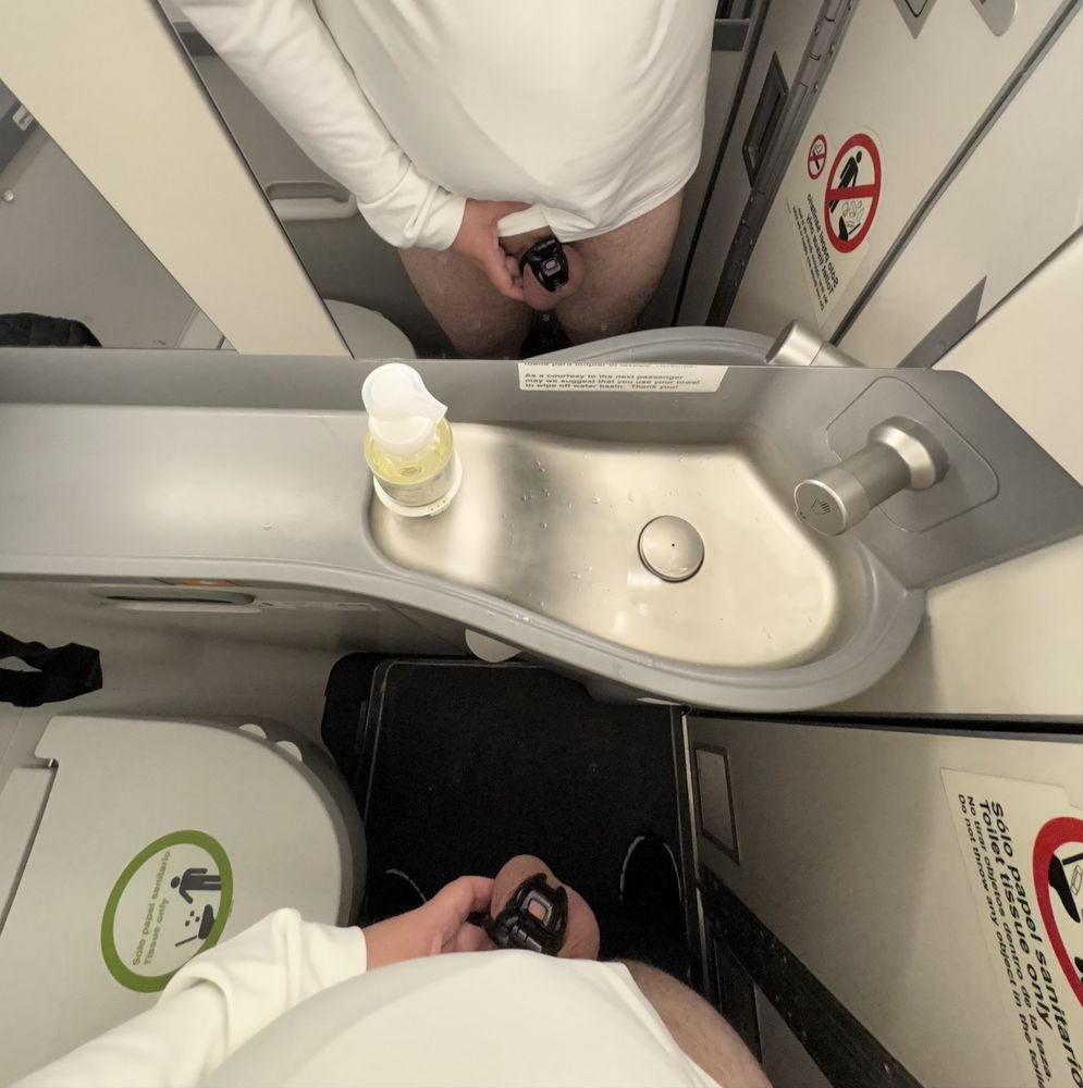 Airplane bathroom selfie showing my caged penis in a Kink3D Baby Cobra chastity cage. The locked penis is shown both in the mirror and live. 