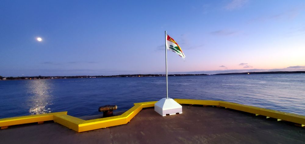 The PEI provincial flag flying from a short, white pole in front of the harbor.