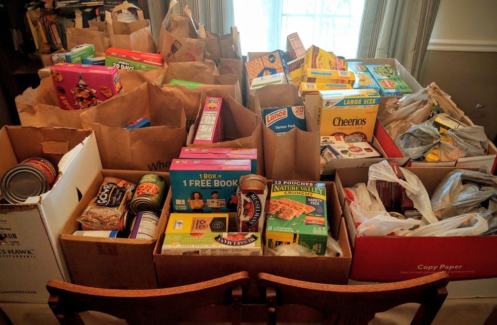 A 6' dining room table filled with boxes and bags of food for a food drive to help replenish a local flood pantry.