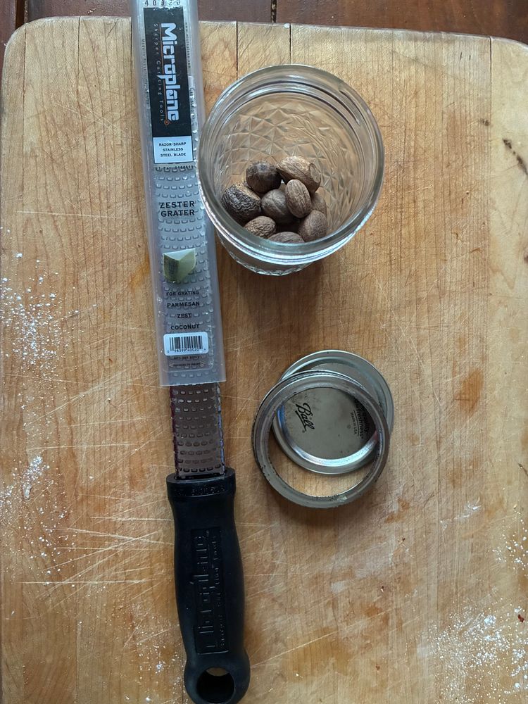 Microplane file, a ball canning jar half full of whole nutmegs, on a wooden cutting board. 