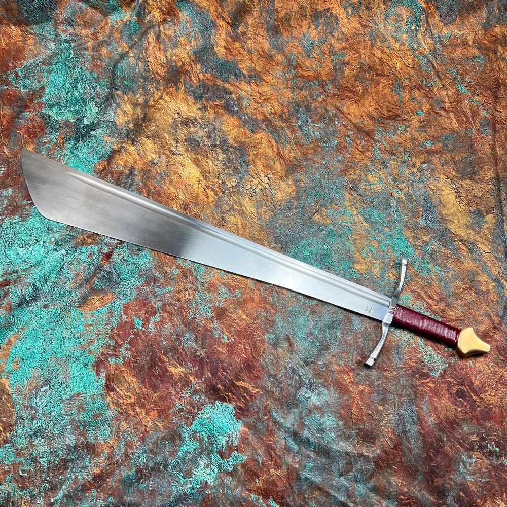 The falchion is a type of European, single-edged medieval sword characterized by a broad blade that is optimized for powerful cuts. It appeared in various forms from the 13th to the 16th century and essentially combined the cutting power of an axe with the handling and versatility of a sword. 

The common misconception though is that they were heavy cumbersome awkward axe-like things. But they are not, they are surprisingly thin and agile. 

Specs below.

 650mm blade 

40mm at the guard swells to 100mm at the widest point

Distal taper approximately 5mm at the guard to 1.2 at the belly 

Leather bound grip 90mm long with bronze pommel 

total length 800mm 

Weight 950grams 

Balances 190mm from the guard 