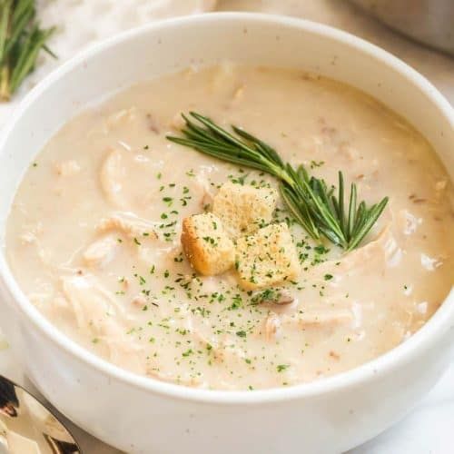A bowl of cream of chicken soup with some croutons and rosemary on top