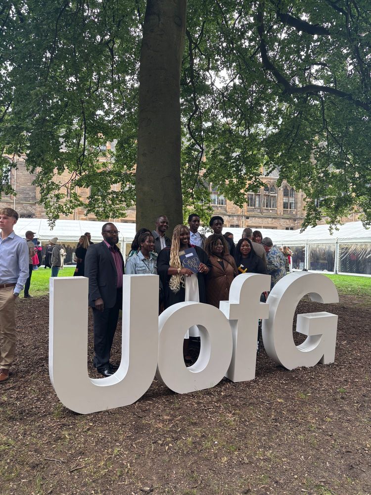 A graduate standing with their family behind big letters which spell out UofG.