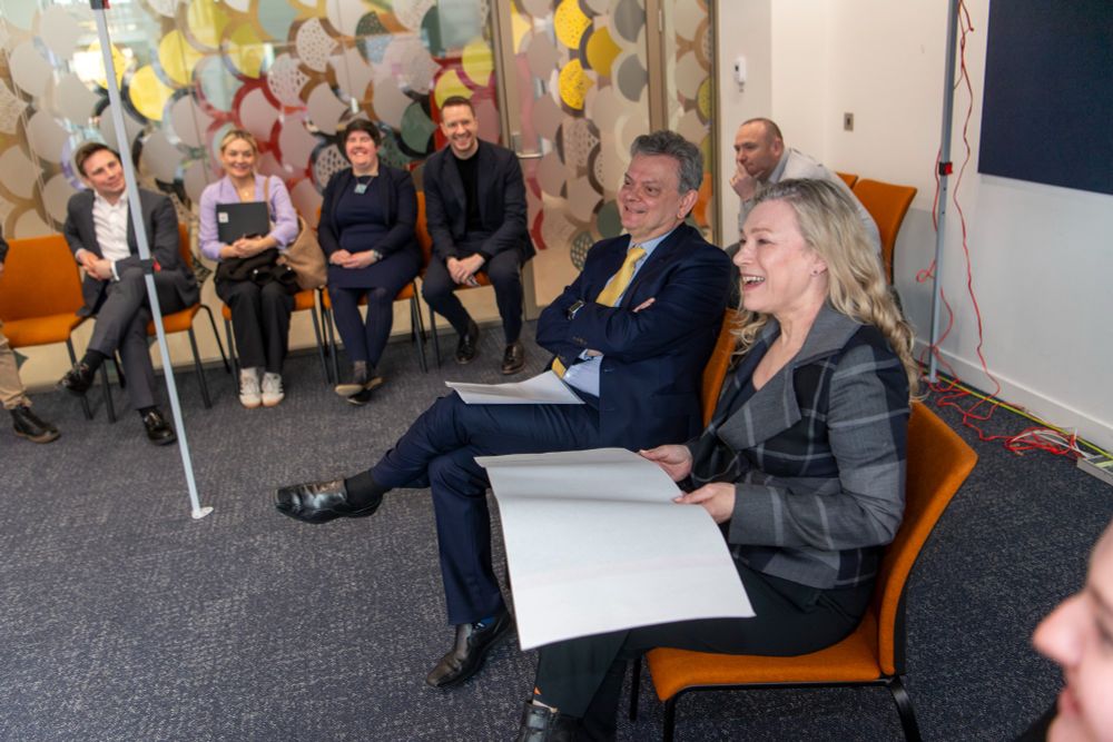 A group of people sit in a semi-circle indoors, smiling and laughing during a discussion, including Gillian Martin MSP and Prof Sir Anton Muscatelli.