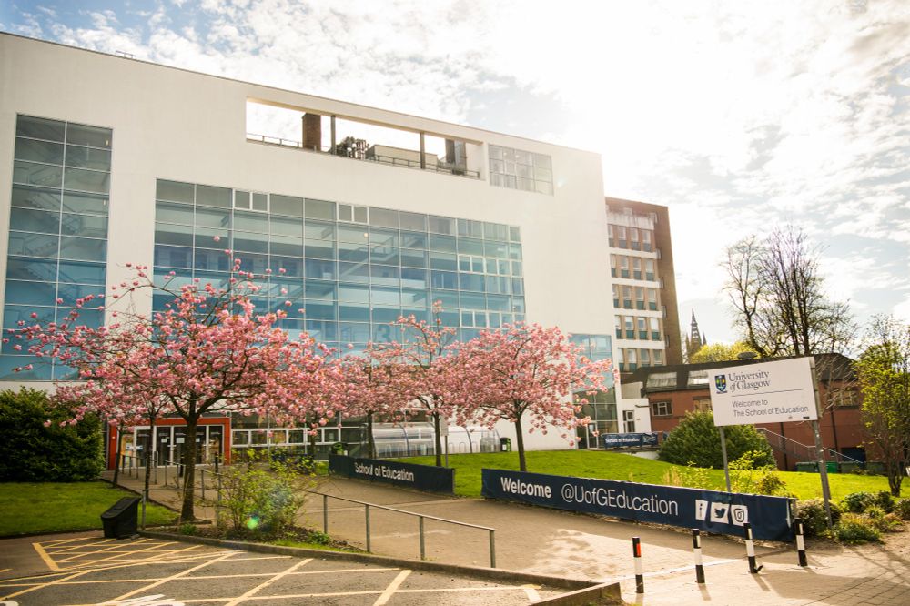The St Andrew’s Building, with blossom on the trees. Blue and white banners read School of Education and Welcome @UofGEducation 