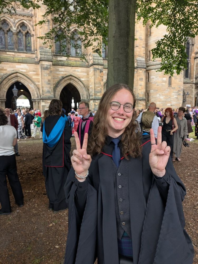 A graduate in the quads holding up the peace sign.