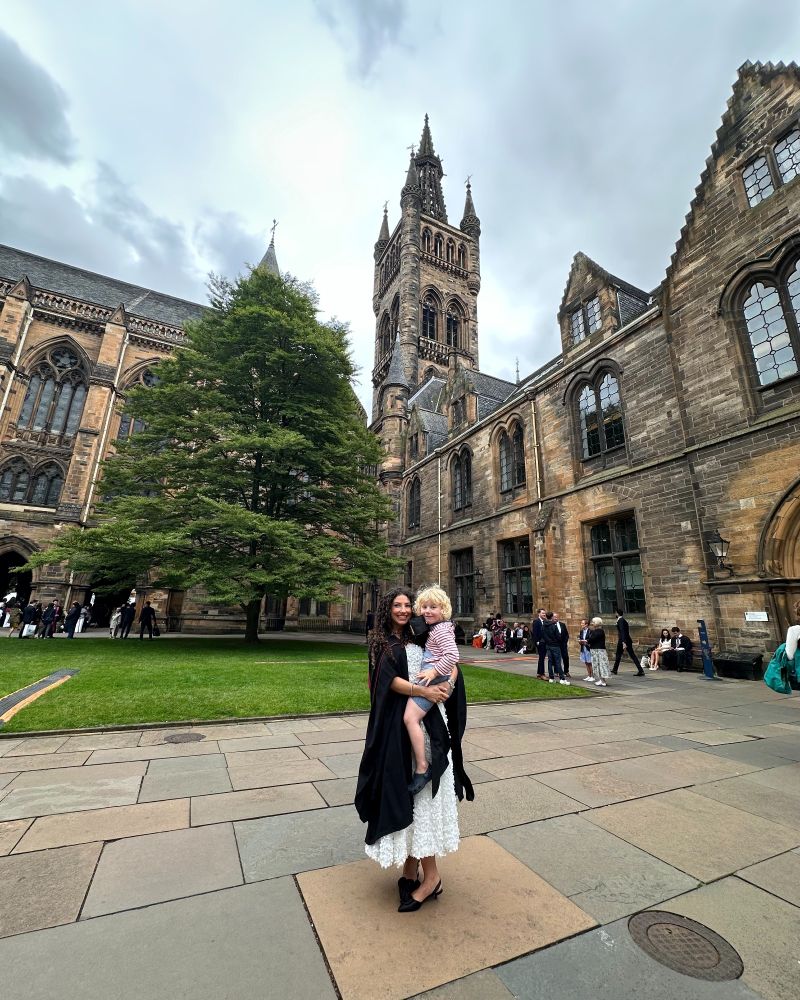 A graduate holding a child with the historic tower in the background.