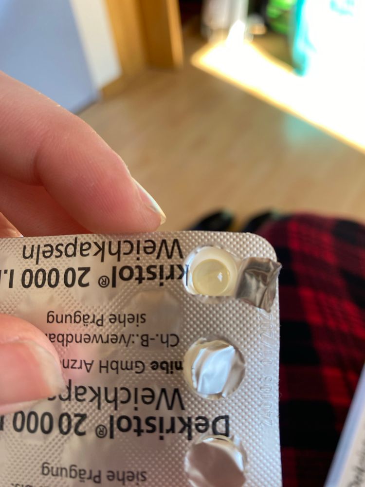 pictured is a vitamin d supplement pill lying inside the open packaging, the pill is round and see through