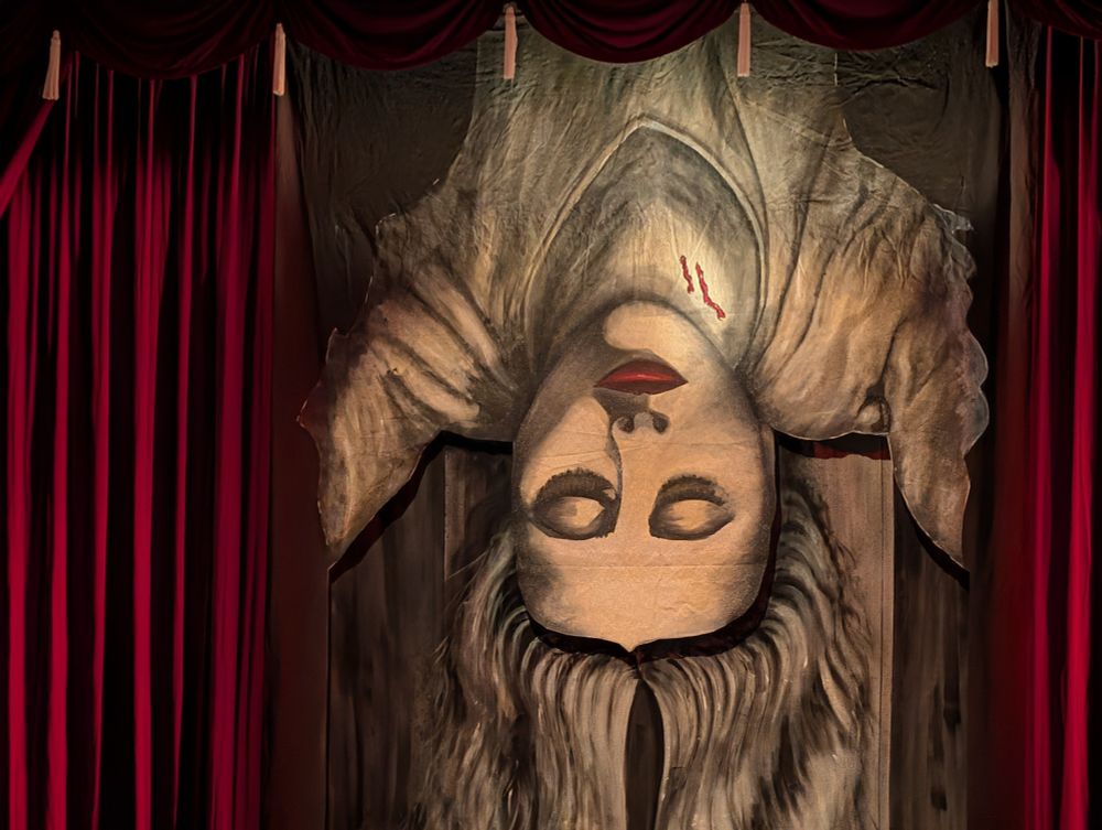 Image of a curtain shaped like a woman hanging upside down, eyes closed, with sepia coloring other than red lips and two red marks on her neck.