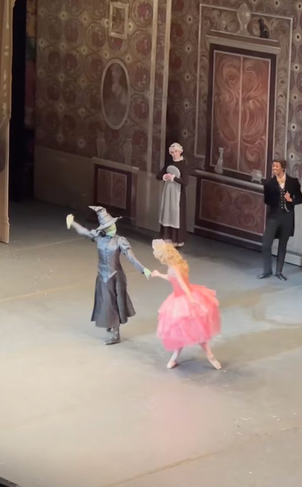 Ballet dancers with Boston Ballet recreating the viral finger-hold interview moment from the Wicked press tour, costumed as Elphaba and Glinda from Wicked. 