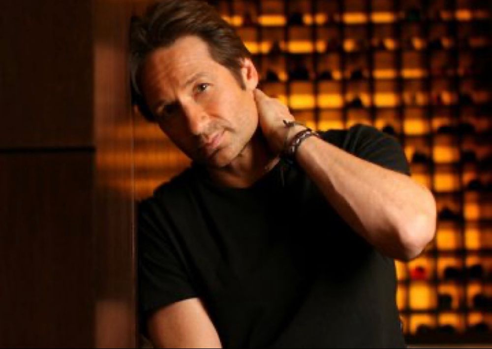 Handsome man dressed in a black shirt leaning against a wall