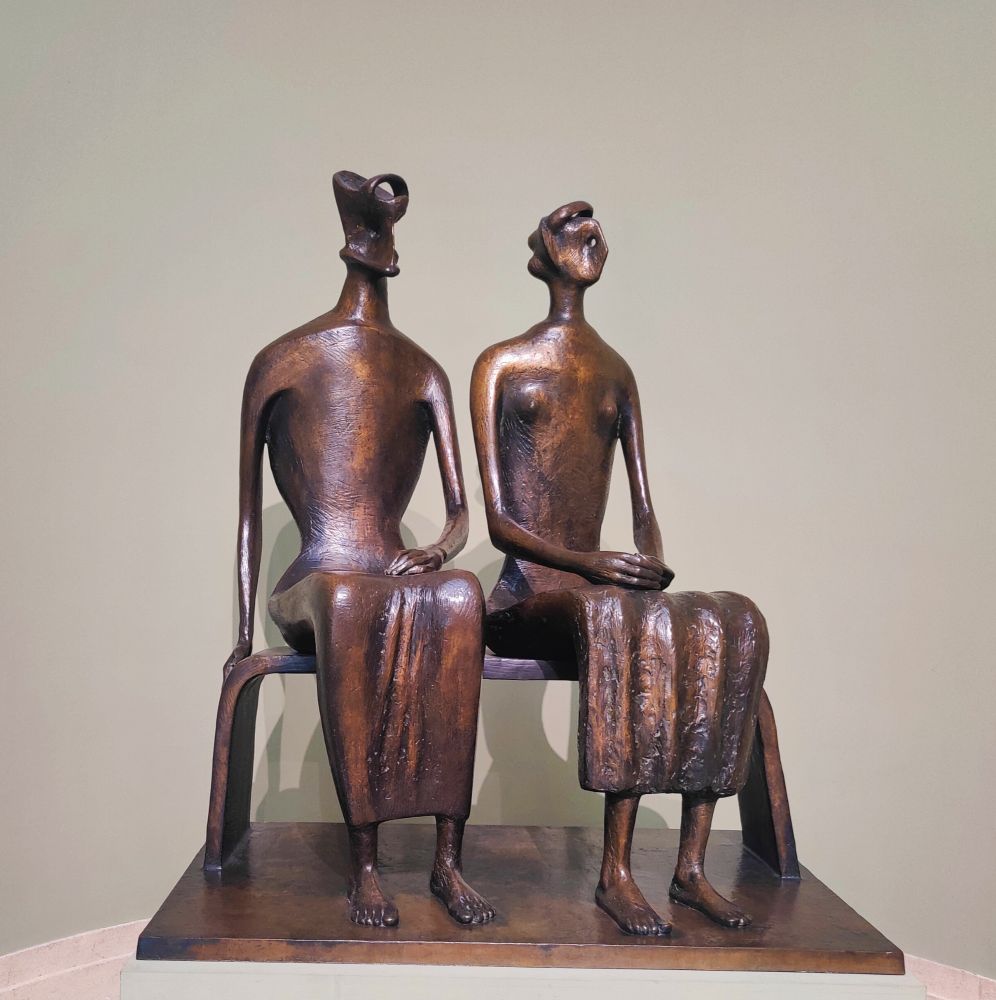 A bronze sculpture of two slightly abstract people sat on a bench