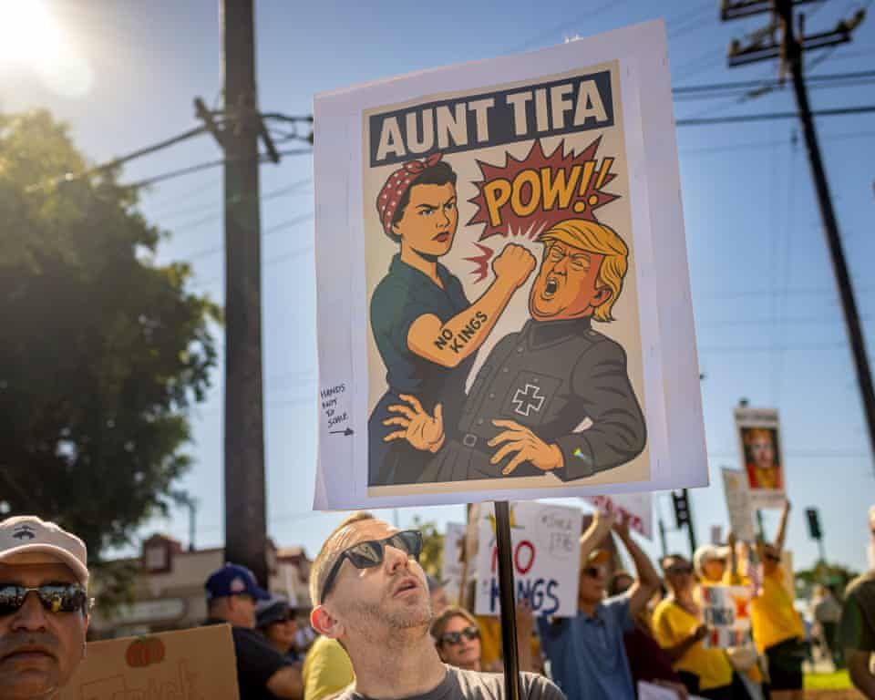 Demonstrator views sign showing 'Aunt Tifa' punching Trump on the nose. Design is akin to WWII poster fighting Fascism - like 'Rosie the Rivetter'... 