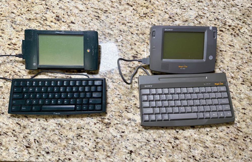 A photo showing two vintage Personal Digital Assistant devices, complete with optional keyboards. On the left is an Apple Newton MessagePad 2100, and on the right is a Sony Magic Link PIC-2000. Both are absolutely awesome. 