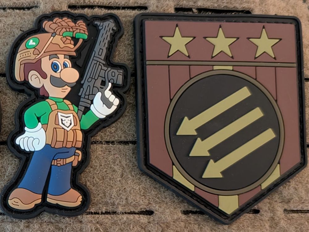 On the left, a PVC patch depicting Luigi in tactical gear holding a short-barreled AR-15 rifle variant. On the right, a second patch depicting the Iron Front USA logo.