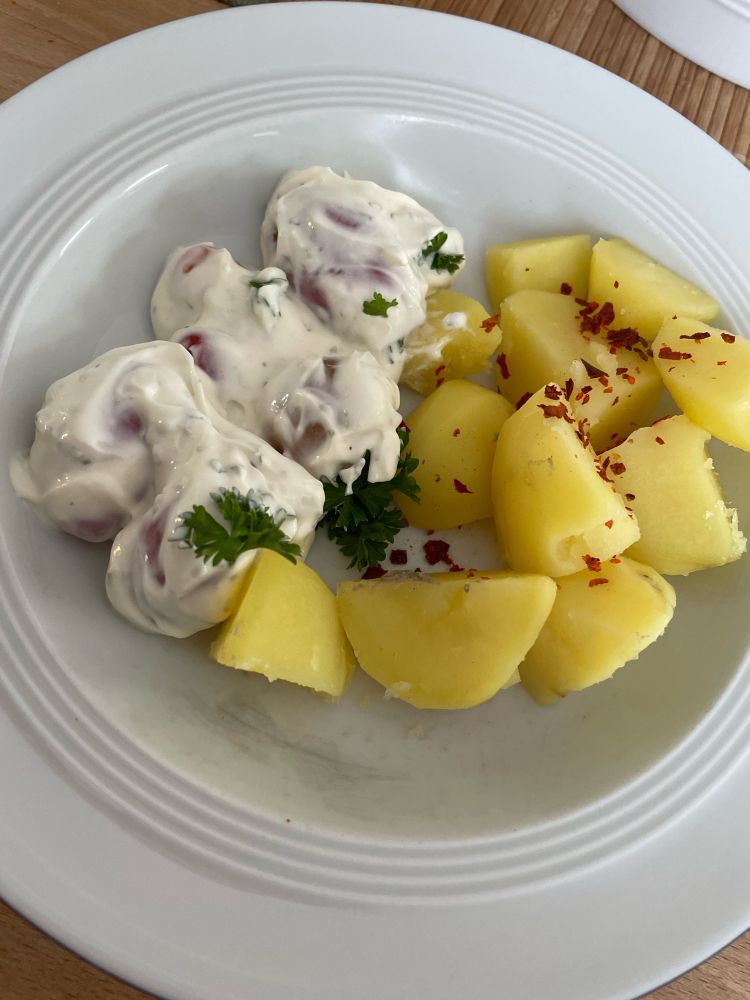 Salzkartoffeln mit Kräuterquark und Tomaten auf einem Teller. Garniert mit Chilliflocken.