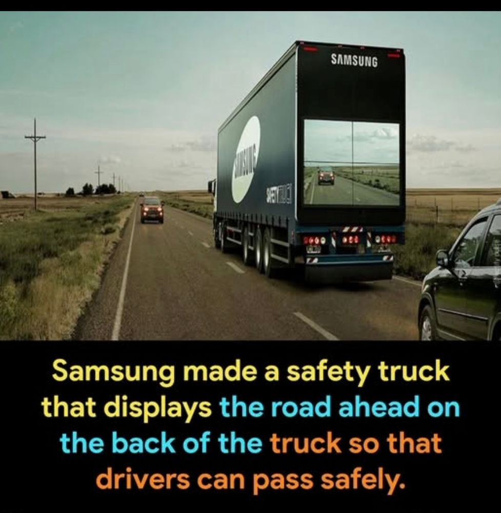 A semi-truck with a screen on the back that shows traffic in front of the truck. 