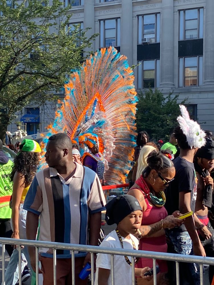 Ovoid orange and cyan feathered masque in a crowd, plus a random person in a fuzzy white bunny mask, because why not