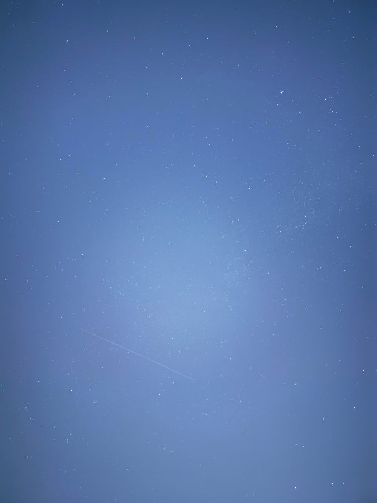 A star field long exposure from the iPhone main camera at 1x zoom. It is not as clear as the 2x zoom on detail, but has a wider angle. A faint shooting star streaks near the center of the frame. 