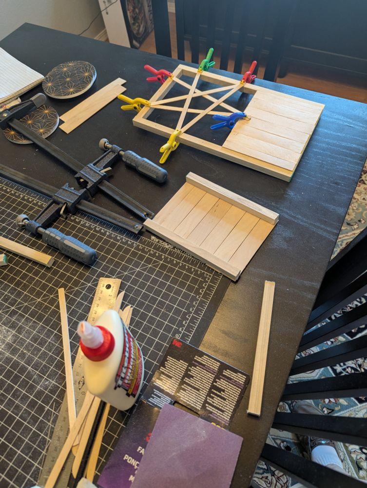 A tabletop covered with a craft project with sticks, sandpaper, wood glue and clamps