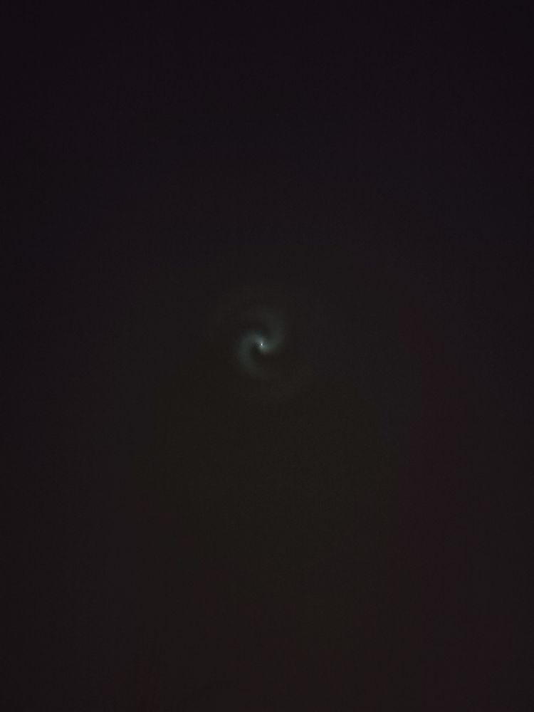 Eine Spiralförmig leuchtende Wolke mit einem Lichtpunkt in der Mitte in einem schwarzen Nachthimmel