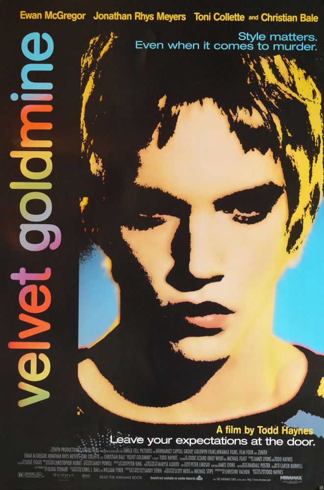 A brightly colored poster for Velvet Goldmine by Todd Haynes featuring a close up of Jonathan Rhys Meyers as Brian Slade. The movie also stars Ewan McGregor, Toni Collette, and Christian Bale. The tagline at the bottom of the poster says Leave your expectations at the door. 