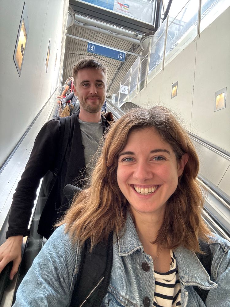 A woman and man smiling together on an escalator at a train station.