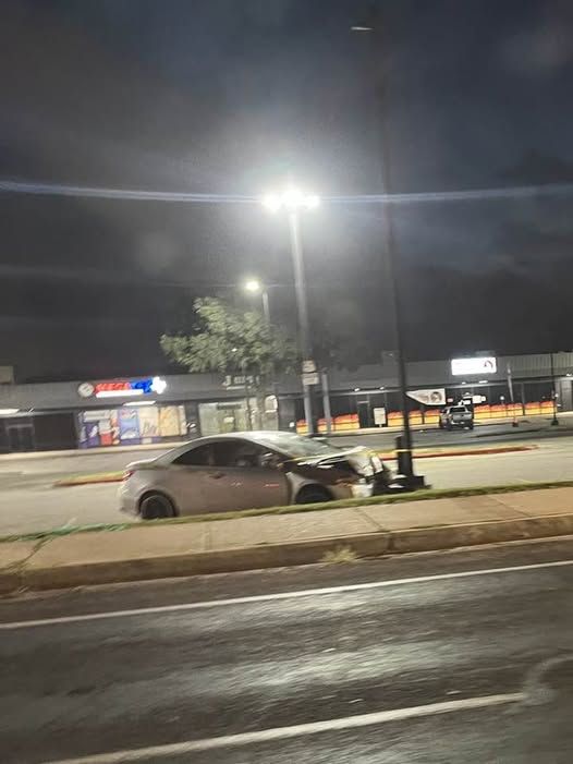 Grey sedan with collapsed front end, smashed up against light pole, in strip mall parking lot. 