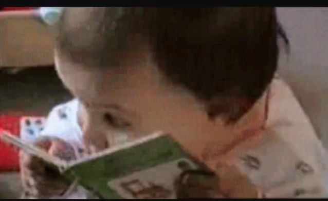 a baby is reading a book with a spoon in his mouth .