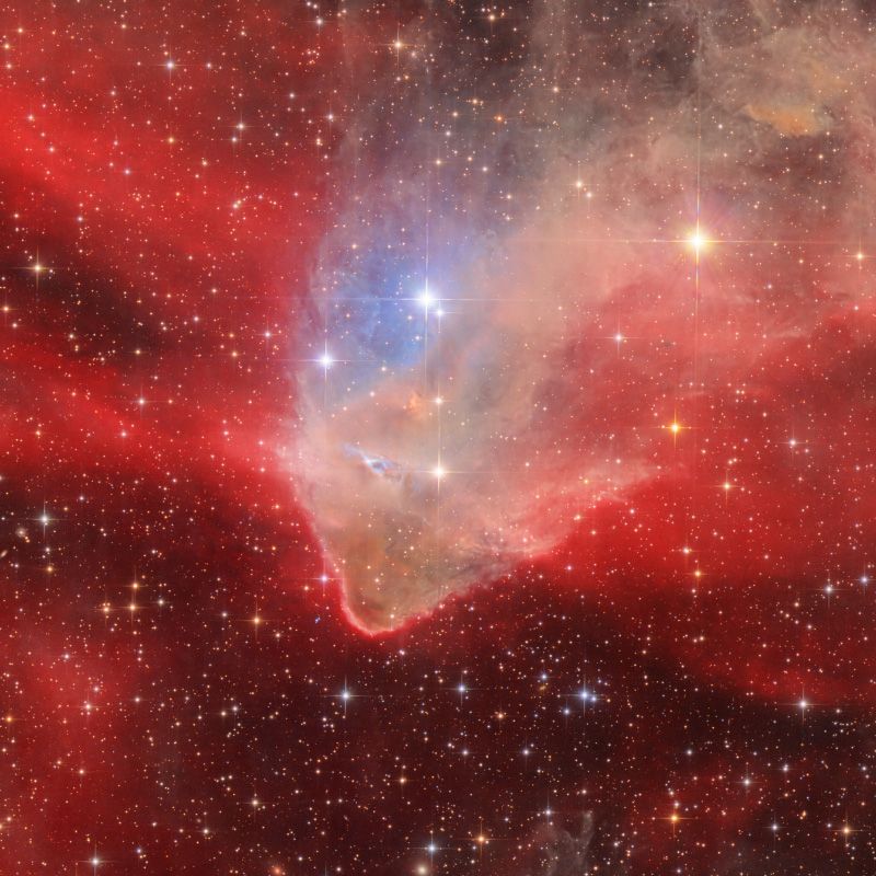A bright brown-white nebula with blue patches in front of a red background speckled with stars