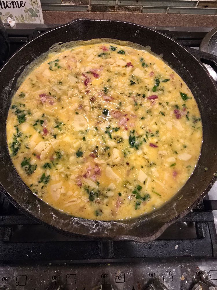 Frittata with cheese, veggies, and bacon, cooking on the stove top in a cast iron pan. 