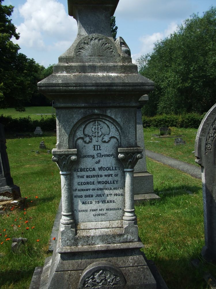 A large pier-style grave monument decorated with classical-style columns at each corner and a relief carving of ivy in a semicircle at the bottom. The inscription on this side reads:

In loving memory of 
Rebecca Woolley
The beloved wife of 
George Woolley 
of Kirkby-in-Ashfield, Notts
Who died July 2nd 1908
Aged 75 years

I know that my Redeemer liveth 