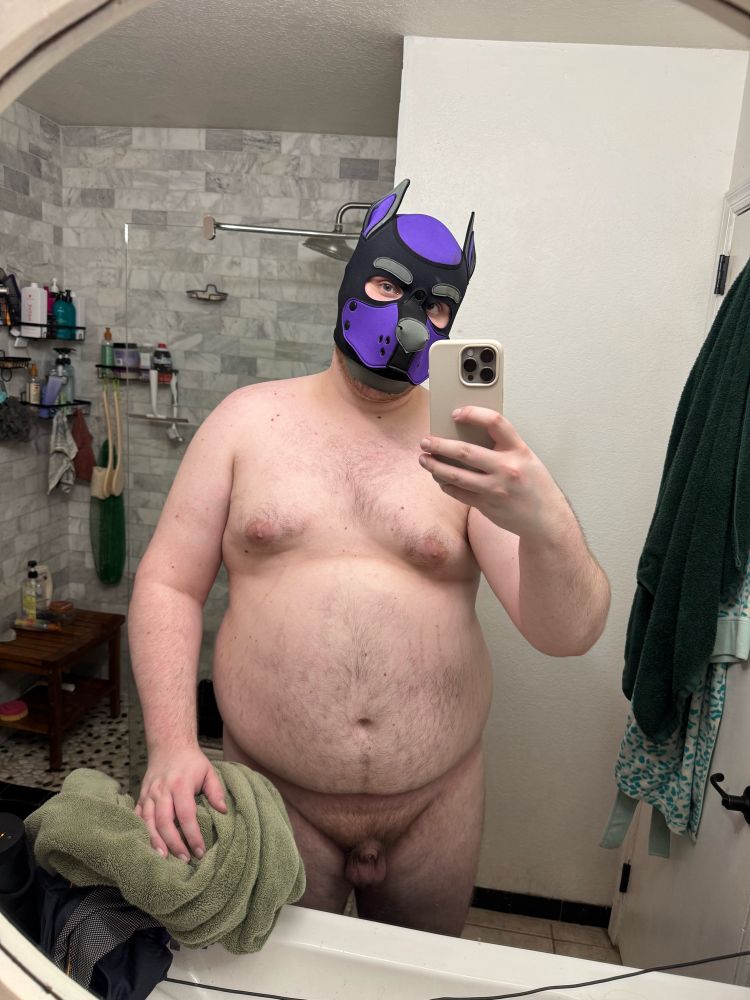 Me standing in front of a bathroom mirror with a towel in my left whilst naked and wearing nothing but my pup hood which is purple, black and grey