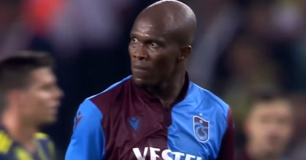 Kızgın bir ifadeye sahip Trabzonspor forması giyen siyahi, iri kafalı adam