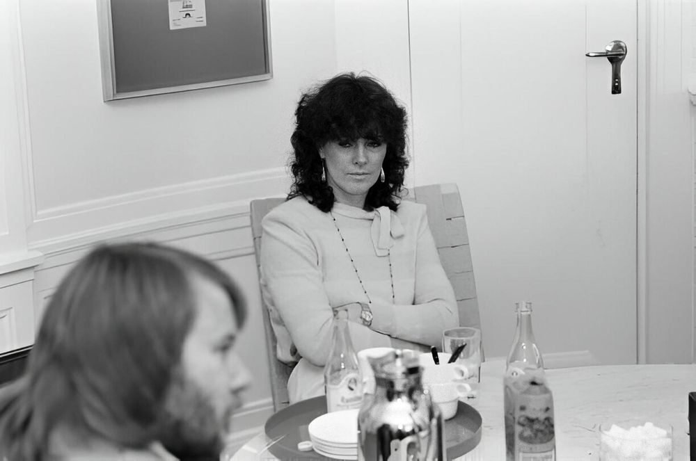 A photo of Anni-Frid Lyngstad from ABBA sitting with her arms folded, apparently looking angrily at Benny Andersson, who is sitting in the foreground of the photo