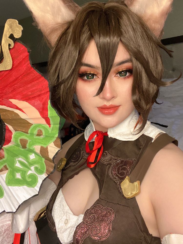 a selfie of me cosplaying tingyun, a honkai star rail character. i am holding a fan next to my face and smiling in a mischievous way. 