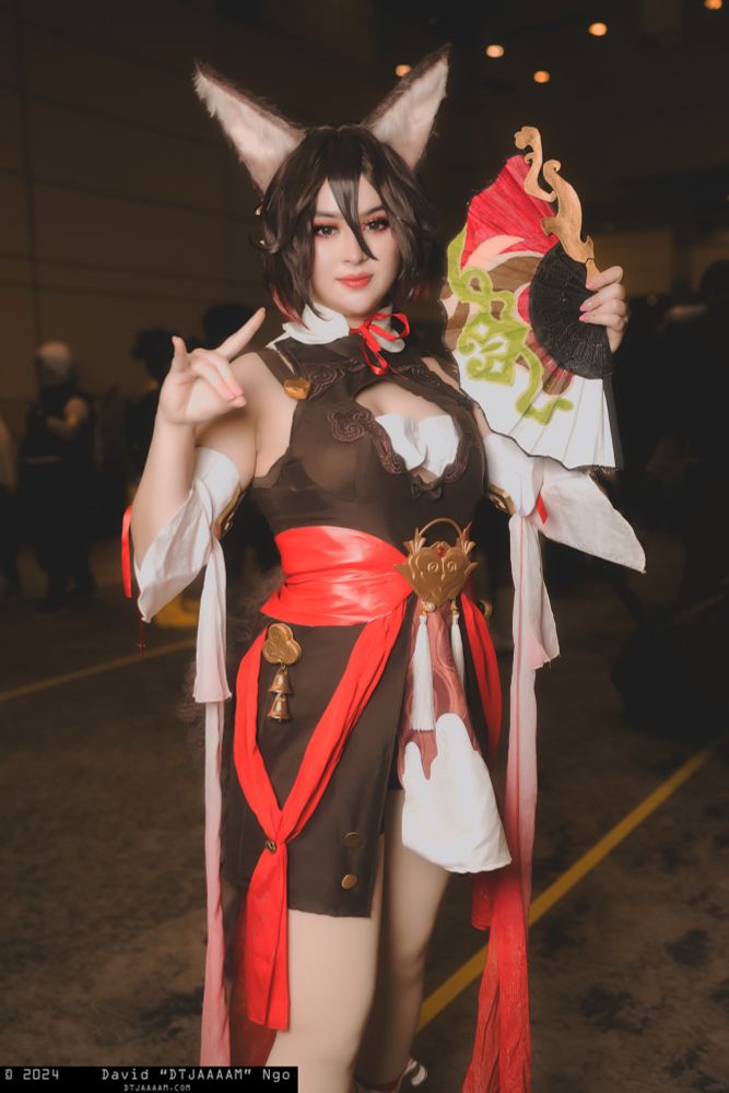 a photo of my cosplaying tingyun from honkai star rail, the picture is full body and i am making a fox gesture with my right hand. i’m holding a fan next to my face and smiling. the photo was taken by david ngo also known as dtjaaaam. 