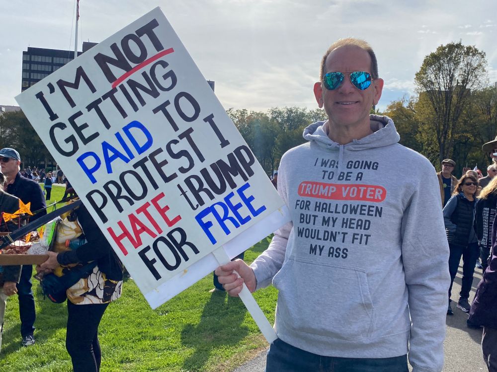 A middle-aged make protestor on the New Haven Green holding a sign reading “I’M NOT GETTING PAID TO PROTEST I HATE TRUMP FOR FREE.” He’s wearing a hoodie that says, “I was going to be a Trump voter for Halloween but my head wouldn’t fit my ass.”