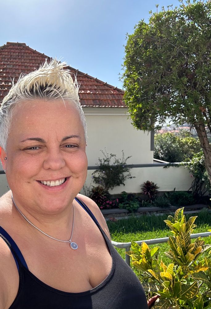 Cristina smiling wearing black vest standing in front garden of parents house in Madeira 