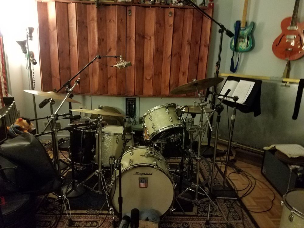 A vintage 1864 Slingerland drumset ready to record at Oxide Lounge Recording. There is a diffusor behind the drums and 2 guitars are seen hanging on the wall.