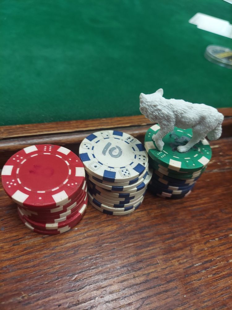 Poker chips with White Wolf topper in the wood bin by green felt