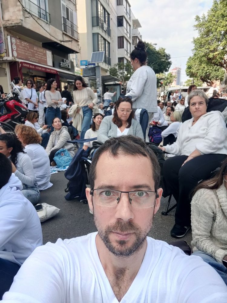 הרבה אנשים לבושים בלבן יושבים על כביש. משמרת 101 למען השבת החטופים 