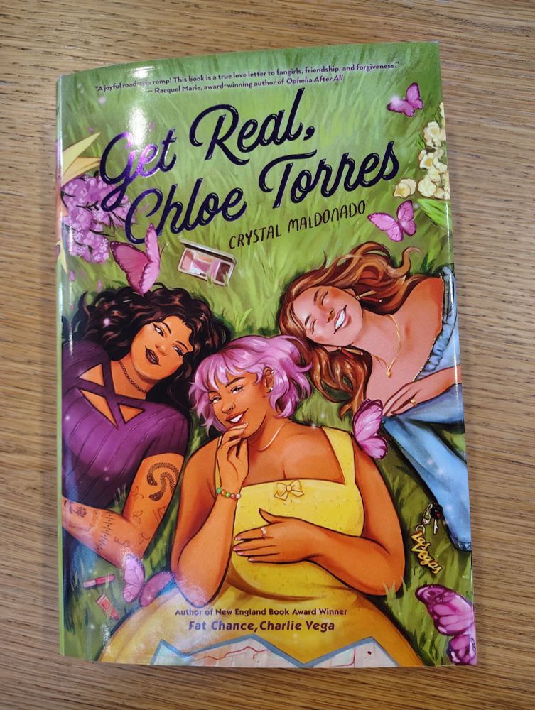 Get Real, Chloe Torres by Crystal Maldonado. The front cover is an illustration of three girls lying in a field, smiling and looking super cute together and surrounded by flowers and butterflies.