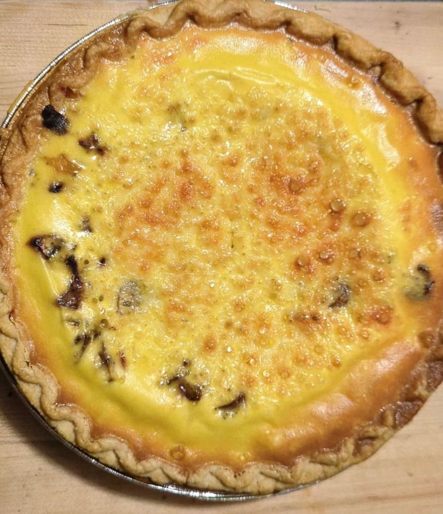 Picture of a freshly baked quiche with light browning on the top. It has mushrooms, shallots and cheese inside.