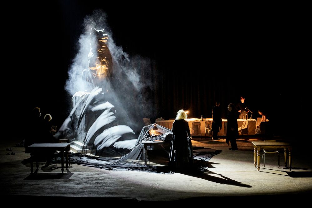 Une femme se dresse devant une grande statue de chienne au centre d'une scène de théâtre.