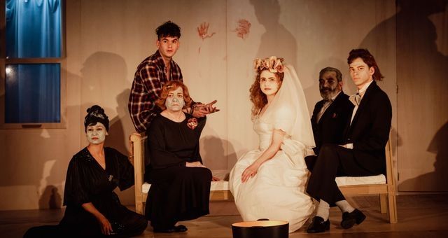 Une famille libanaise en habits de cérémonie de mariage regarde le public ; la plupart sont assis sur un lit en bois.