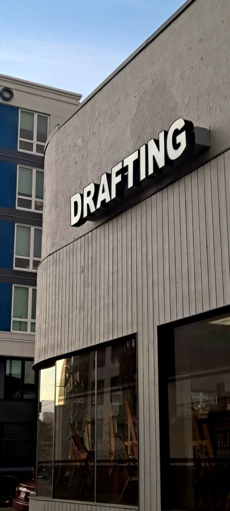 A sign reads "Drafting" on the side of a building in the city. 